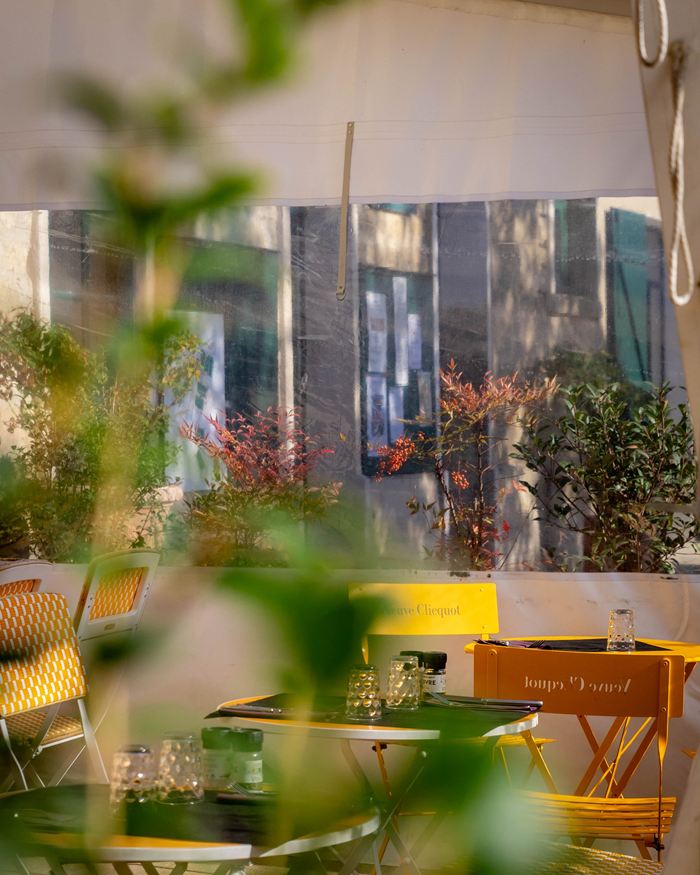 Tables et chaises jaunes sur la terrasse couverte, derrière un feuillage